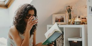 Γυναίκα πίνει τσάι και διαβάζει στο κρεβάτι της