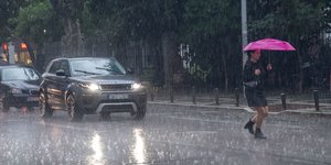 Γυναίκα περνά δρόμο με ομπρέλα κάτω από βροχή