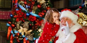 Ένα χαμογελαστό κοριτσάκι αγκαλιάζει τον Άγιο Βασίλη με φόντο ένα χριστουγεννιάτικο δέντρο