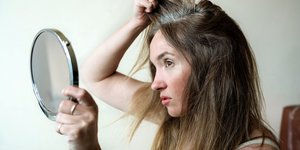 Νεαρή γυναίκα κοιτά στον καθρέφτη τα γκρίζα της μαλλιά