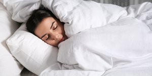 Γυναίκα κουκουλωμένη στο κρεβάτι με λευκό πάπλωμα