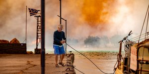 Άνδρας στη Χίο προσπαθεί να δέσει τη βάρκα του με φόντο την πυρκαγιά 