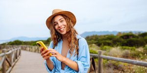 Χαμογελαστή ταξιδιώτισσα κρατά ένα κίτρινο κινητό