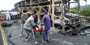 Εθελοντές απομακρύνουν τραυματία από το αποτεφρωμένο λεωφορείο στη νότια Ινδία