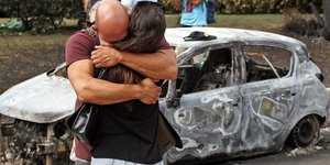 άνδρας γυναίκα αγκαλιά μπροστά από καμένο αυτοκίνητο μετά από φωτιά στο Μάτι