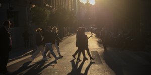 Άνθρωποι περπατούν σε δρόμο της Αθήνας υπό το φως του απογευματινού ήλιου 