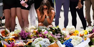 Μια γυναίκα γονατίζει και προσεύχεται μπροστά στο ανθοστόλιστο μνημείο για τα θύματα του μακελειού στην παραλία Bondi του Σίδνεϊ 