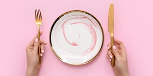 Γυναίκα με μαχαιροπίρουνα και άδειο πιάτο σε ροζ φόντο