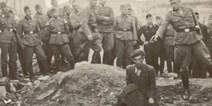 Ένας άνδρας γονατιστός στο χείλος ενός λάκκου γεμάτου πτώματα, κι ένας Γερμανός στρατιώτης με το χέρι σηκωμένο, το πιστόλι να ακουμπά σχεδόν τον σβέρκο του / WIKIPEDIA