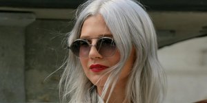 Νεαρή γυναίκα με λευκή μπλούζα, μαύρη τσάντα, γυαλιά και γκρίζα μαλλιά