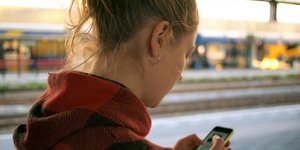 κοπέλα με καρέ πανωφόρι κοιτάζει το κινητό της