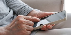 Senior woman's hand operating a smartphone - Shutterstock