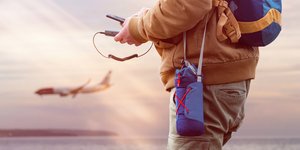 Τουρίστας κρατά στα χέρια του ένα power bank και φορτίζει ένα smartphone κατά τη διάρκεια του ταξιδιού με φόντο αεροπλάνο
