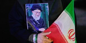 Υποστηρικτής του Αλί Χαμενεΐ κρατάει τη φωτογραφία του Ανώτατου Ηγέτη του Ιράν και μια σημαία