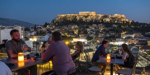 Κόσμος απολαμβάνει το ποτό του σε ταράτσα μαγαζιού με θέα την Ακρόπολη