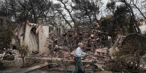 Μια γυναίκα στο Νέο Βουτζά ρίχνε νερό στην αυλή του σπιτιού της που έχει καταστραφεί-Φωτογραφία: ΑΡ/Yorgos Karahalis